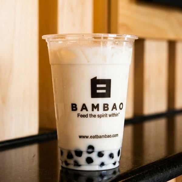 A BambaO bubble tea with tapioca pearls sits on a reflective black counter against a wooden wall.