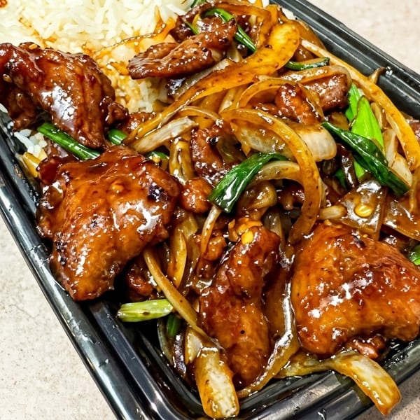 Sweet and sour chicken with onions and green onions, served with white rice in a black takeout container.