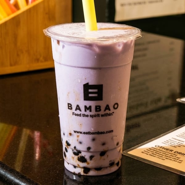 A purple taro bubble tea from Bambao with a yellow straw on a dark counter.
