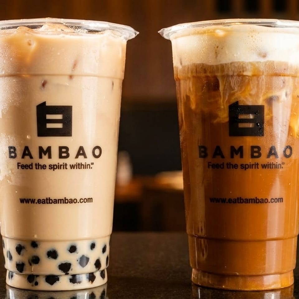 Two Bambao drinks, one light-colored with boba and one dark-colored with foam, on a dark surface.
